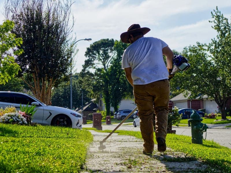 Jardinero recortando el césped frente a una casa